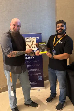 Team member Rejah exchanges his new book with a cybersecurity veteran, Len Moe, at c0c0n.