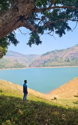 A team member posing for a click with the scenic backdrop of Thenmala reservoir behind him.